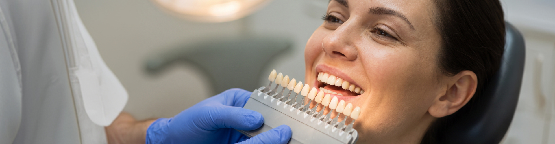 Woman smiling while a dentist holds a shade guide against her teeth to select a veneer color.